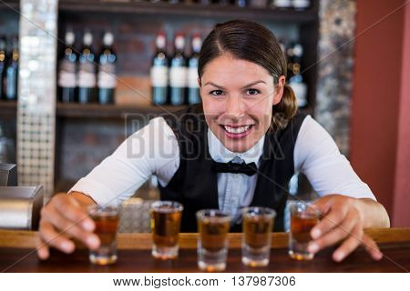 Portrait of bartender placing shot glasses in a row on bar counter in bar