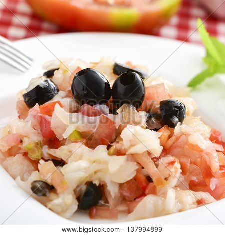 closeup of a dish of esqueixada de bacalla, a cold dish made with codfish, red pepper, tomato, onion and black olives, and dressed with olive oil, typical of Catalonia, Spain, on a table