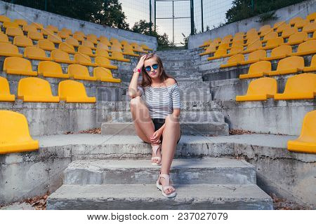 Fashionable Woman With Round Glasses Sitting On The Steps Of The Stadium Outdoor