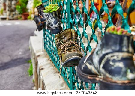 Old battered boots with lace rope used as decorations for shabby metal fence.