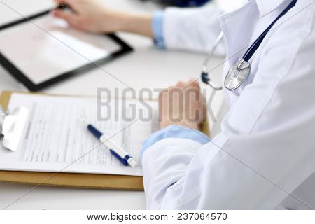 Closeup Of Stethoscope. Female Doctor Is Busy While Sitting At The Desk In Hospital. Cardiologist Ch