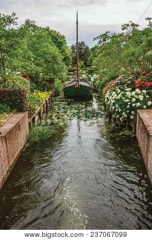 Charming Small Canal With Decorative Boat Next To Lush And Flowery Garden In Cloudy Day At Drimmelen