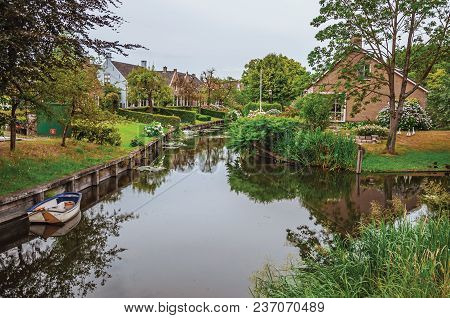 Charming Small Canal Next To Rustic Houses With Lush Gardens And Trees Reflected On The Water In Clo