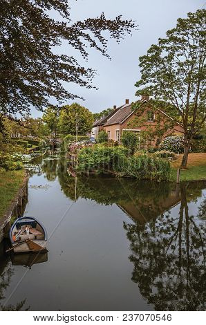 Charming Small Canal Next To Rustic Houses With Lush Gardens And Trees Reflected On The Water In Clo