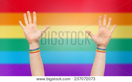lgbt, same-sex relationships and homosexual concept - close up of male hands wearing gay pride awareness wristbands over rainbow background
