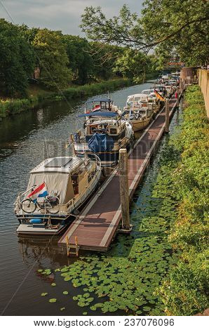 Trees, Aquatic Vegetation And Boats Anchored In Pier On The Bank Of The River Dommel And Blue Sky In