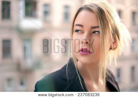 Portrait Of A Young Woman In A Black Suit Close-up Against A Background Of A Blurry City In The Rays