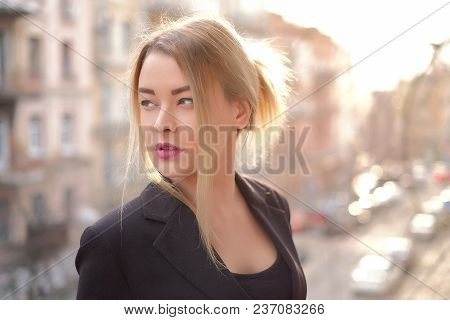 Portrait Of A Young Woman In A Black Suit Close-up Against A Background Of A Blurry City In The Rays