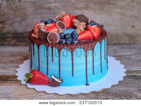 Beautiful Homemade Cake With Blue Cream And Chocolate Glaze, Decorated With Strawberries And Blueber