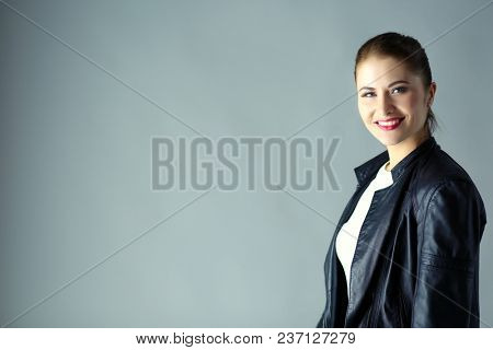portrait of beautiful young brunette woman in stylish black jacket on gray.