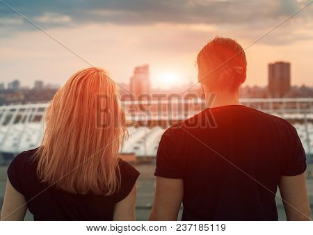 Two Lovers Embracing Overlooking The City At Sunrise Sunset. Romantic Setting.