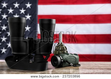 Military Monocular, Binocular And Grenade On Table Against American Flag Background