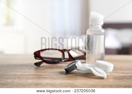 Contact Lens Case, Tweezers, Bottle Of Solution And Glasses On Table