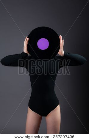 The Girl In Biack Holds A Vinyl Disk In Her Hands, Closes Her Face. Studio Photography On A Gray Bac