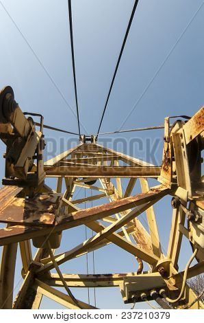 Arm Of Crane. Yellow Boom Of An Old Crane On A Blue Sky Background. An Unusual Perspective.