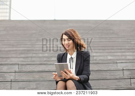Businesswoman Sitting On Stairs With Tablet. Concept Of Working In Open Ait And Modern Technology, B