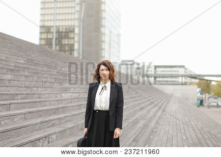 Successful Businesswoman Standing On Stairs With Bag And High Buildings In Background. Concept Of Pr