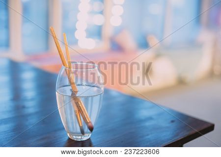 Paint Brushes In A Glass Of Water. Blue Background