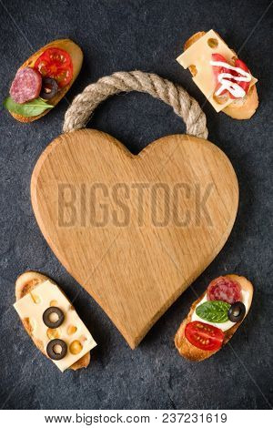 Open faced sandwich canape or crostini on a wooden serving board on dark stone  background closeup. Top view.