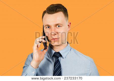 Portrait Of Young Businessman Dressed In Blue Shirt And Tie Talking On The Mobile Phone, Isolated On