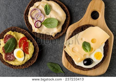 Open  faced  sandwich canape or crostini on a wooden serving board on dark stone background closeup. Top view.