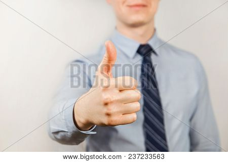 Young Businessman Dressed In Blue Shirt And Tie Shows Thumb Up Close Up, On Gray Background