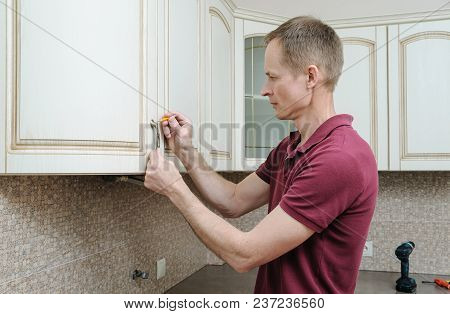 Installation Of Kitchen Furniture. The Man Is Marking With A Pencil To Fix The Door Handle Of The Ca