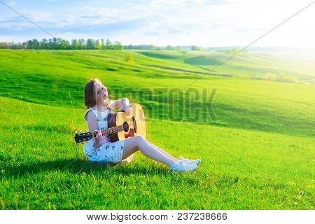Left-handed Irl Playing Guitar Outdoor On Green Spring Grass Meadow.