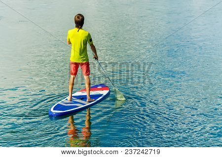 Sup Surfing Man Stand Up Paddle Boarder Paddling At Sunset On River.