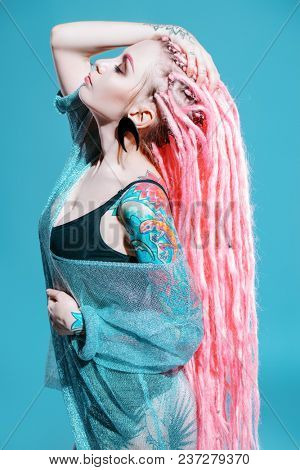 Sexy girl with pink dreadlocks posing in kombidress on a gray background. Beauty, fashion.