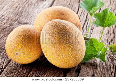 Ripes melons with melon leaves on wooden background.