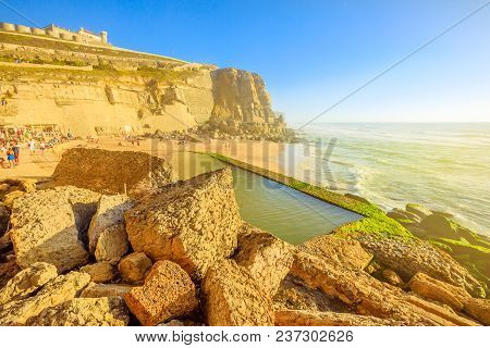 Scenic Promontory And Beach At Sunlight Of Azenhas Do Mar With Famous Natural Pool Visible At Low Ti