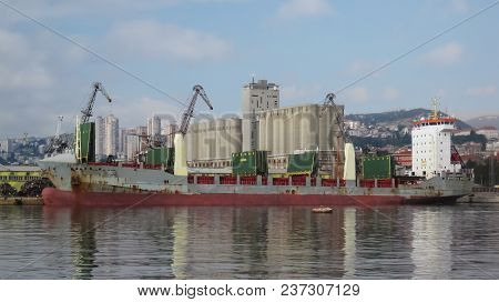 Aft Of Red,huge Cargo Ship In Port Of City Rijeka At Cloudy Summer Day |crane|derrick