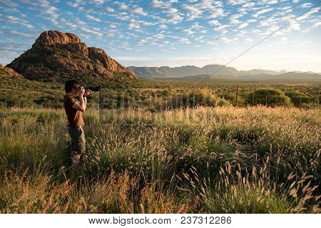Young Asian Male Photographer Taking Photo Of Beautiful Sunrise In Savanna (savannah) Woodland, Nami