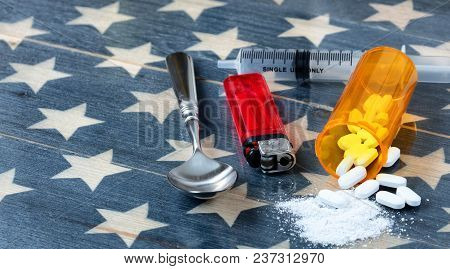 Front View Of Opioid Pain Killer Tablets With Spoon, Lighter And Syringe On Rustic Usa Flag In Backg