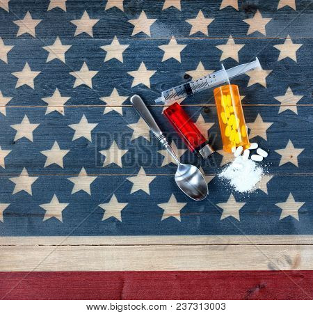 Overhead View Of Opioid Pain Killer Tablets With Spoon, Lighter And Syringe On Rustic Usa Flag In Ba
