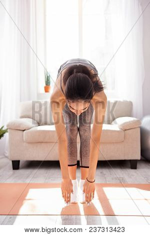 Perfectly Supple. Athletic Young Woman Bending Forward And Touching The Floor While Working Out In T