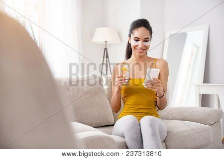 Mood-boosting Message. Upbeat Young Woman Texting On Her Mobile Phone And Drinking Water While Sitti