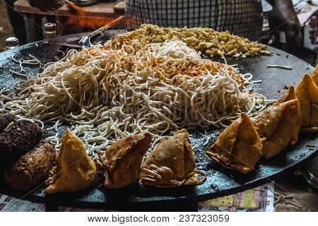 Fried Samos Noodles And Other Street Food On A Large Black Pan. Typical Street Food In India. Man Is