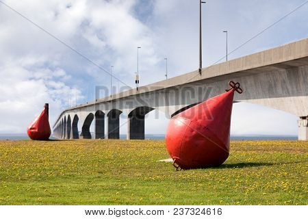 Giant red metal buoys on the grass infront of the eight mile long Confederation Bridge, that links Prince Edward Island with New Brunswick, Canada. 