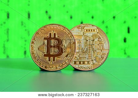 Two Gold Bitcoins Lie On The Green Surface On The Background Of The Display, Which Shows The Process