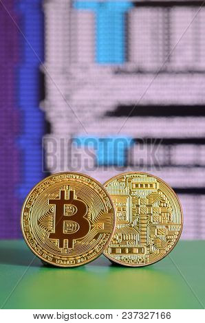 Two Gold Bitcoins Lie On The Green Surface On The Background Of The Display, Which Shows The Process