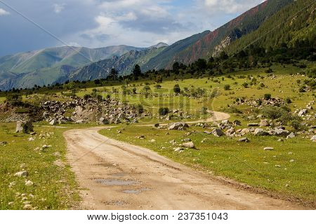 Colorful View Of Green And Snowy Mountains With Elbrus Summit Under Fluffy White Clouds.