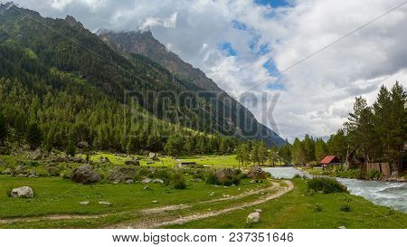 Colorful View Of Green And Snowy Mountains With Elbrus Summit Under Fluffy White Clouds.