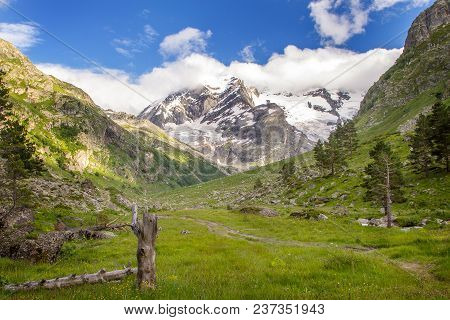 Colorful View Of Green And Snowy Mountains With Elbrus Summit Under Fluffy White Clouds.