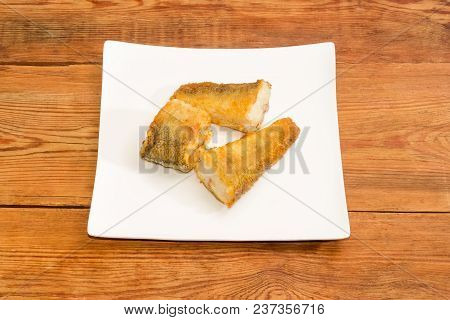 Three Slices Of The Fried Saltwater Fish Notothenia On A Square Dish On An Old Rustic Table