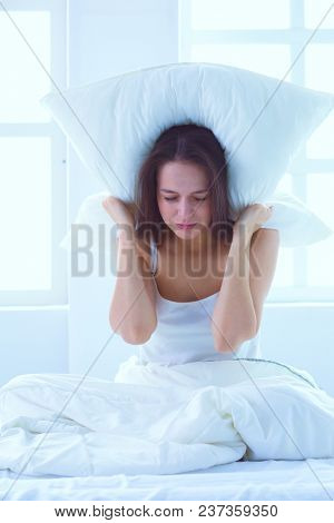 Young caucasian woman covering her head and ears with pillows