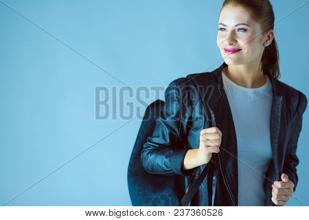 portrait of beautiful young brunette woman in stylish black jacket on gray.