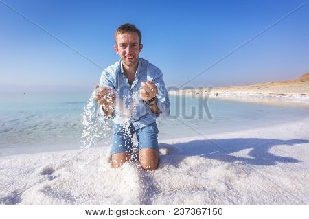 Ttourist Throws Salt Sitting On The Shore Of The Dead Sea. Jordan Landscape