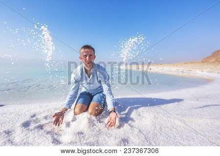 Ttourist Throws Salt Sitting On The Shore Of The Dead Sea. Jordan Landscape